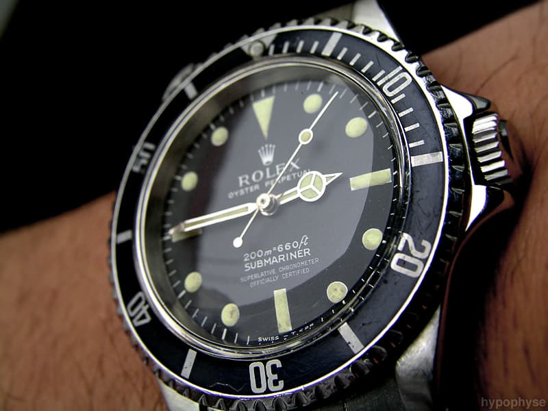 Rolex Submariner 5512 on the wrist: matte black dial with white print, depth rating reading meters first (“200m=660ft”), four-line chronometer text, “Swiss – T<25” at six and no chapter ring; rounded crown guards. · Photo: hypo.physe (Flickr) · CC BY-SA 2.0 · https://creativecommons.org/licenses/by-sa/2.0/ · Source: https://www.flickr.com/photos/hypophyse/4436618998/